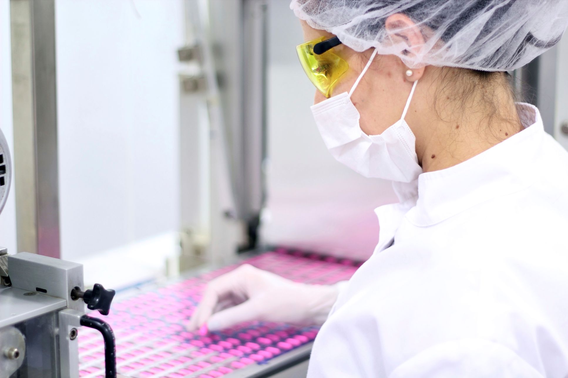 Pharmacist wearing hair net, safety glasses, face mask, gown, and gloves while handling medication.