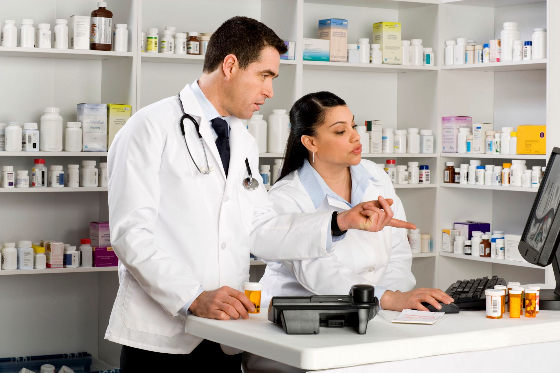 Pharmacist and tech looking at a computer monitor in a pharmacy.