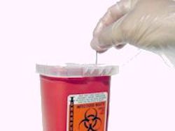 Gloved worker placing a needle in a SHARPS container.