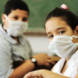 Two children sitting in a classroom both wearing masks with a chalkboard in the background.