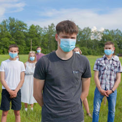 Group of children standing socially distanced in a grassy field. All of the children are wearing masks.