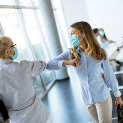 Two women wearing masks greet each other with an elbow bump.