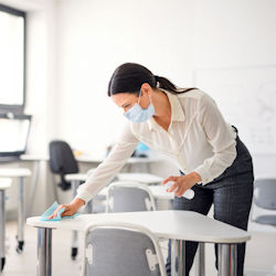 Woman in a mask wipes down a school desk with disinfectent.