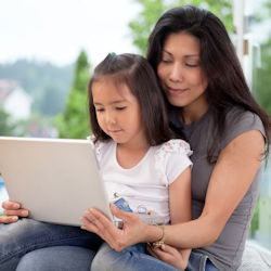 Child sits on adults lap. They are looking at a computer tablet together