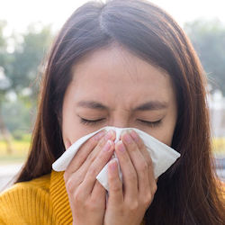 A woman outside blows her nose into a tissue.