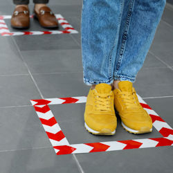 person wearing yellow shoes stands in a square that has been marked with tape on the floor