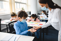 Teacher spraying hand sanitizer in student's hands.