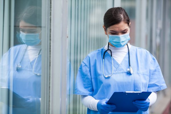 A woman, wearing scrubs and a face mask, lokking at a chart.