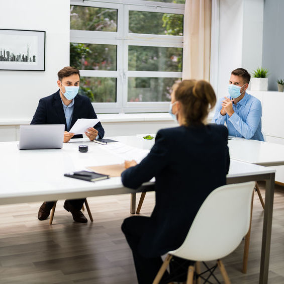 Three people sitting around a table each wearing a face mask.