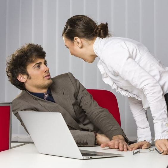 Woman standing and yelling at a man who is sitting in a chair. The man is leaning away from the woman.