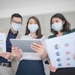 A man and two  woman wearing face masks look at a tablet. The two people on either side are holding reports.