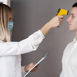 A woman wearing a face mask uses a forehead thermometer to take a man's temperature