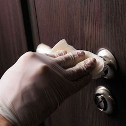 A gloved hand uses a wipe to clean a a door knob.