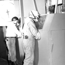 Two workers painting within an enclosure