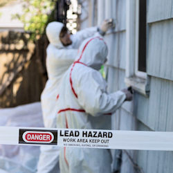 Two workers outside of a house removing paint