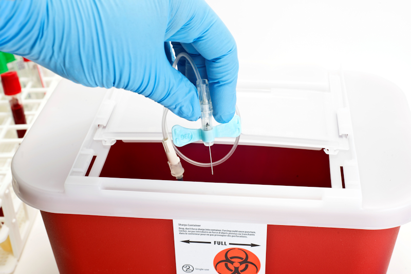 Gloved worker dropping a needle into a SHARPS container