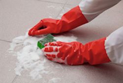 Worker wearing PPE while scrubbing the floor with a sponge.