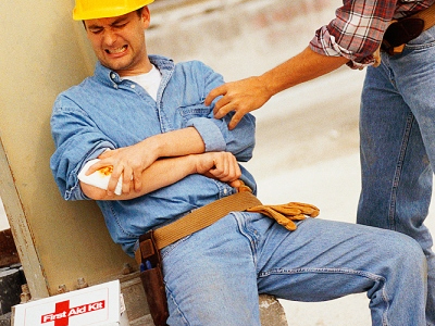 worker with an arm injury being assisted by another worker and a first aid kit nearby.