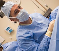 Surgeon wearing scrubs and mask in an operating room.