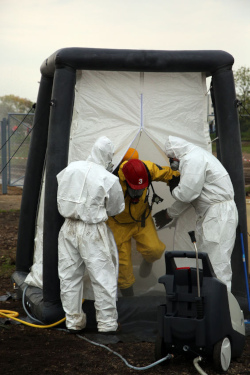 Two workers helping a third worker out of a decomination tent