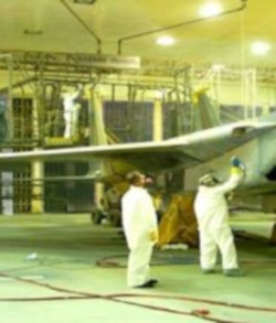 Two painters in PPE using a paint sprayer can to paint a plane.