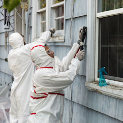 Two workers removing lead paint from the outside of a building