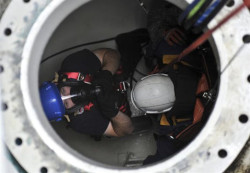 Two workers in a confined space with harnesses and breathing aparatuses.