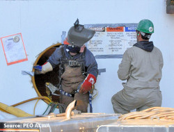 Confined space attendant stationed outside the work space with one worker preparing to enter confined space