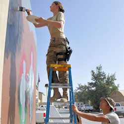 worker standing on a ladder using both hands to paint a wall