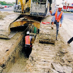 Worker in a trench walking under heavy equipment