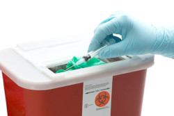 Sharps container with gloved hand inserting used needle