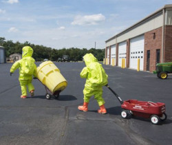 Workers in Level A protective suits moving a hazardous waste barrel