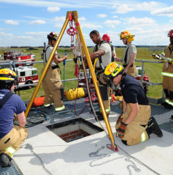 Rescue tripod, winch, and retrival lines above a confined space. There is a group of rescuers around the tripod for training.