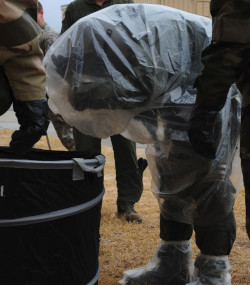 A man removes his overcape during decontamination training.