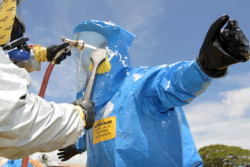 A person in a blue Level A protective suit being scrubbed to remove contaminants. The person doing the scrubbing is wearing a white protective suit and respirator.