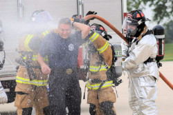 Group of workers in protective suits use water to wash off an exposed person not wearing protective clothing.