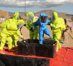 Group of people, in yellow protective suits, help a person, in a blue protective suit, into a decontamination station.