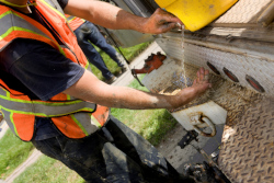 Man in a dark shirt and a orange safety vest uses water in a jug to wash his hands.