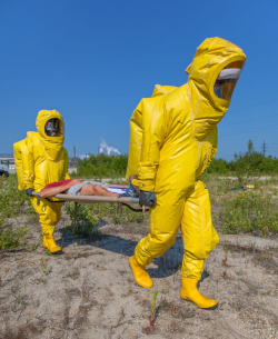 Two men in yellow hazmat suits carry a man on a stretcher.