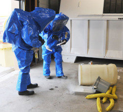 Two workers in blue hazmat suits stare down at the ground.