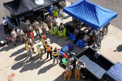 A large group people stand under and around a couple of pop up canopies