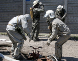 Four workers in silver protective suits. Three of the workers have hard hats with hoods.