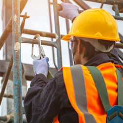 Worker climbing a ladder on scaffold has PPE and is using fall arrest equipment