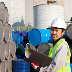 Worker holding notebook in front of many drums classifying chemicals