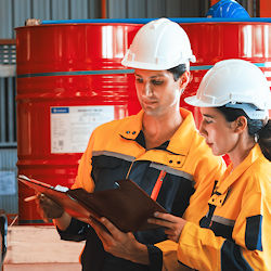 Two workers outdoors standing in front of drums analyzing chemical hazard data