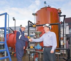 A worker and supervisor shaking hands outside in front of tanks