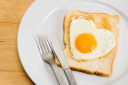 Fried egg in the shape of a heart on toast on plate with silverware.