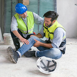 One employee kneeling next to another who is in pain holding his knee.