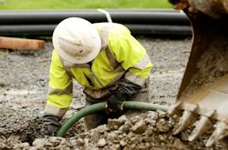 Worker pushing hose into a pit wearing PPE including a hard hat