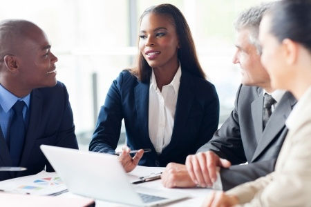 Four employees meeting around a table with a open computer on it.